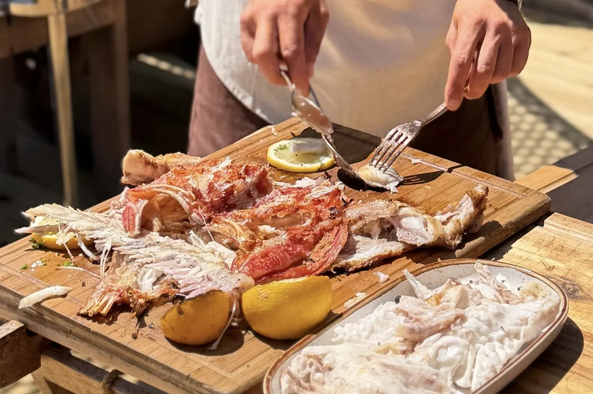 A chef plating fresh seafood on a wooden board at Comporta Café Beach Club, Portugal.